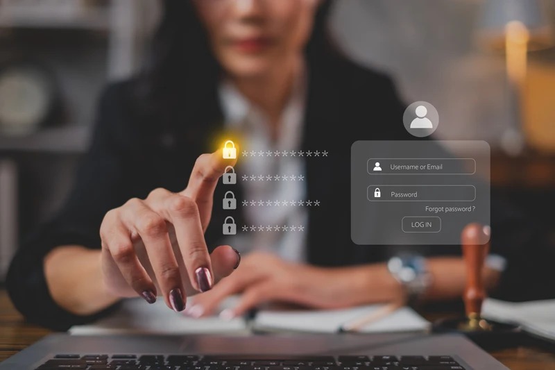 Imagem de uma mulher usando um computador para fazer login em uma conta, com campos de senha visíveis e um ícone de bloqueio destacado, representando segurança digital.