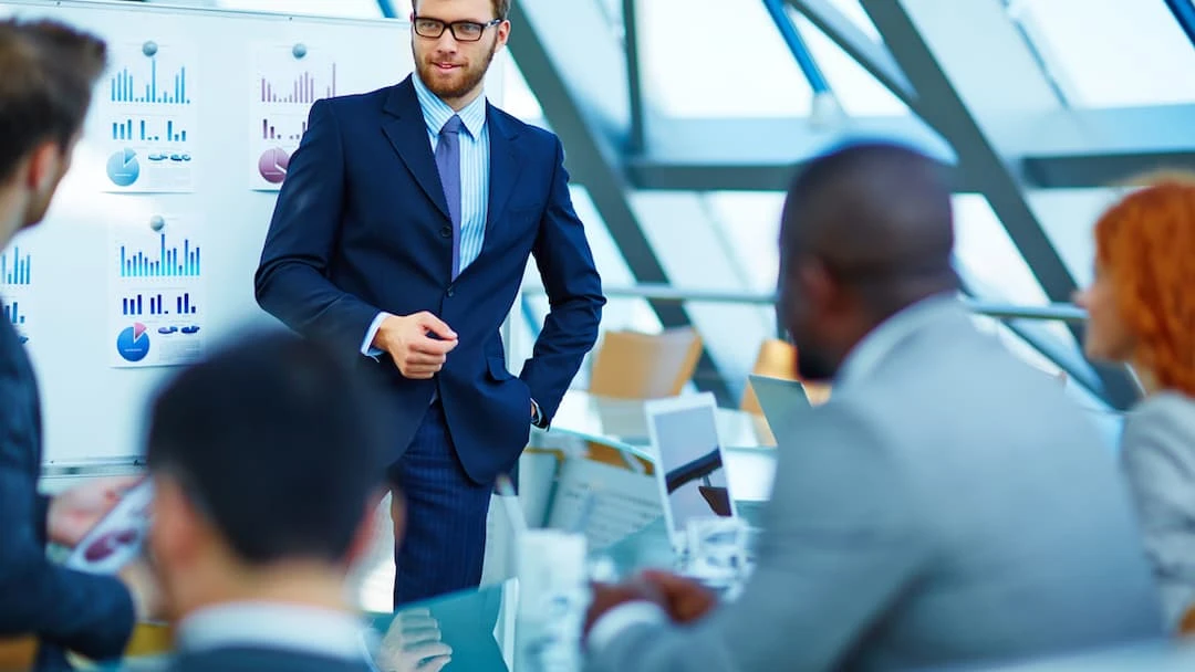 Homem apresentando gráficos em reunião de negócios, com foco em liderança e comunicação eficaz. Ambiente moderno, ideal para treinamento profissional.