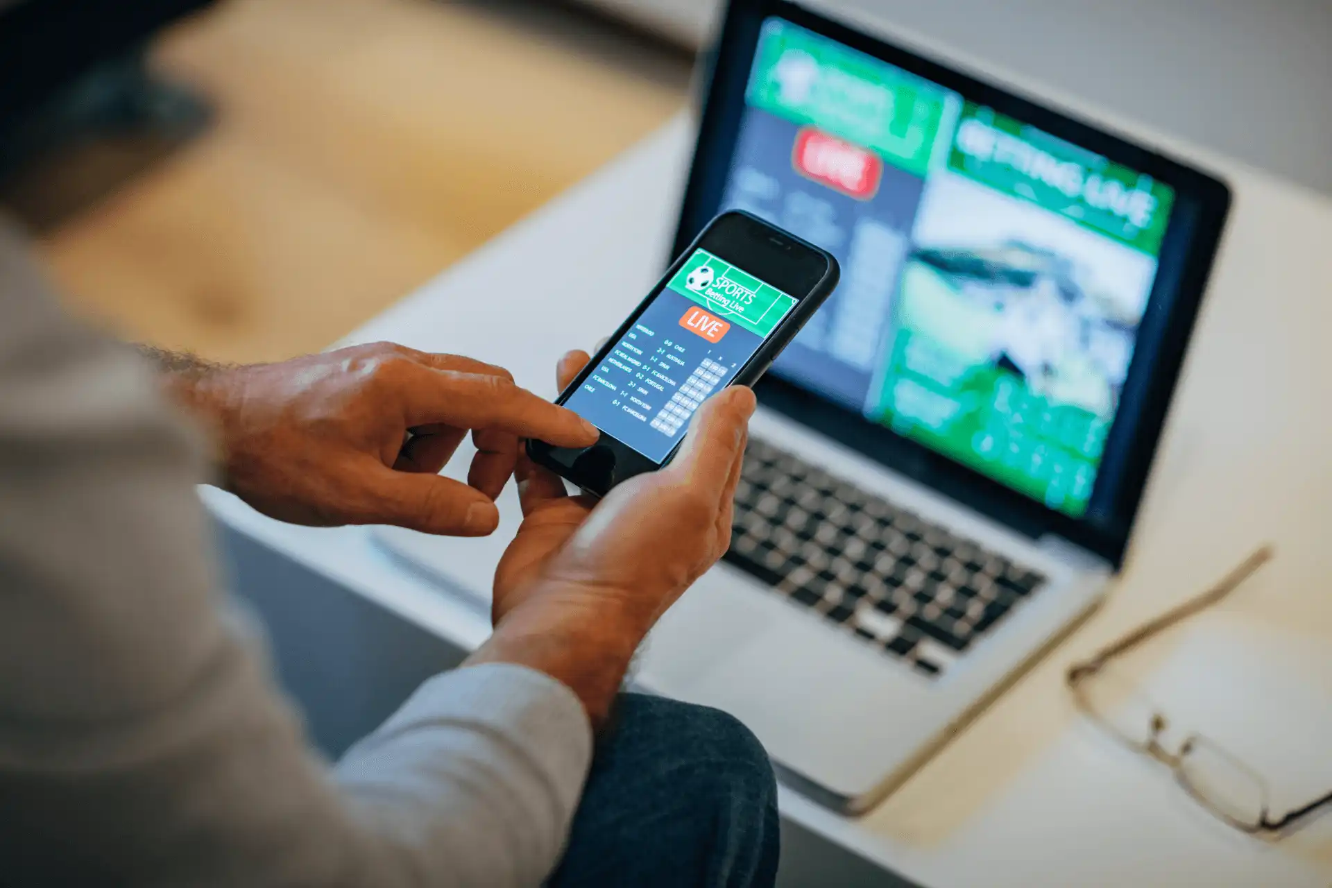 Pessoa utilizando um smartphone e um laptop para apostas ao vivo, destacando a interatividade e a tecnologia em plataformas de apostas esportivas.