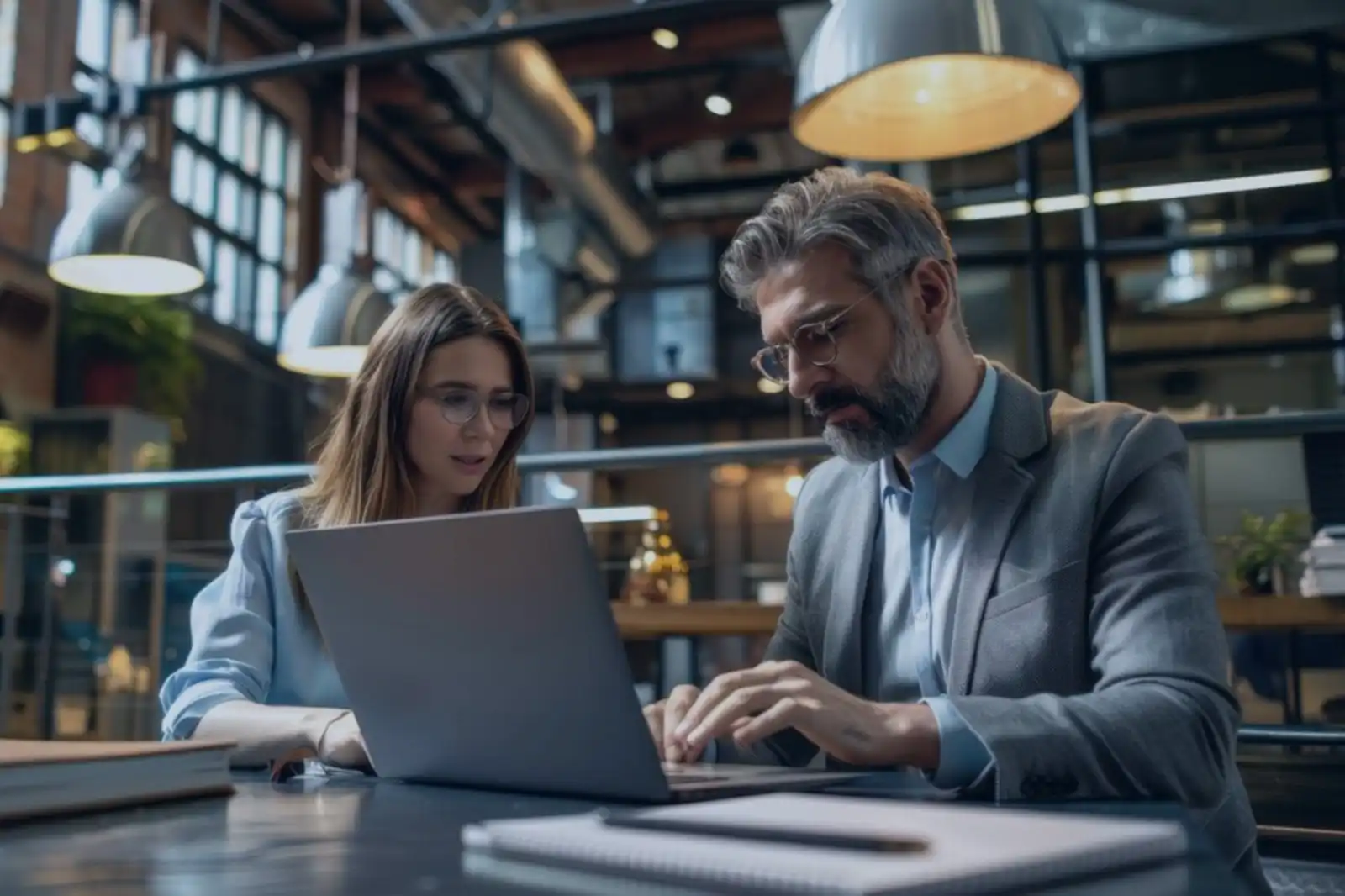 Profissionais trabalhando em um escritório moderno, analisando informações em um laptop. Colaboração e produtividade no ambiente de trabalho.
