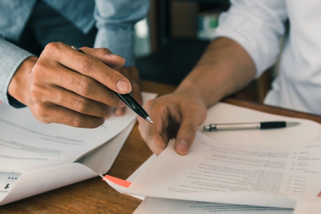 Mãos de profissionais discutindo documentos e assinando contratos em um ambiente de escritório, simbolizando a importância da formalização de acordos.