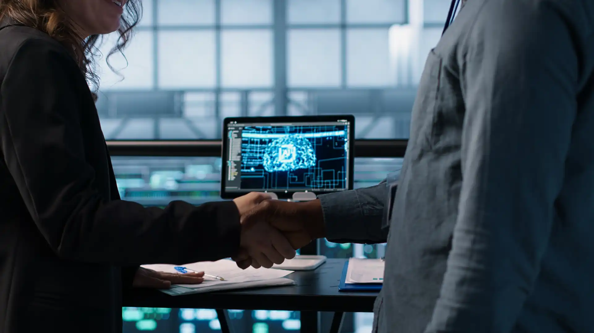 Imagem de duas pessoas apertando as mãos em um escritório moderno com uma tela de computador exibindo gráficos e dados, simbolizando auditoria interna inteligente com inteligência artificial Vennx.