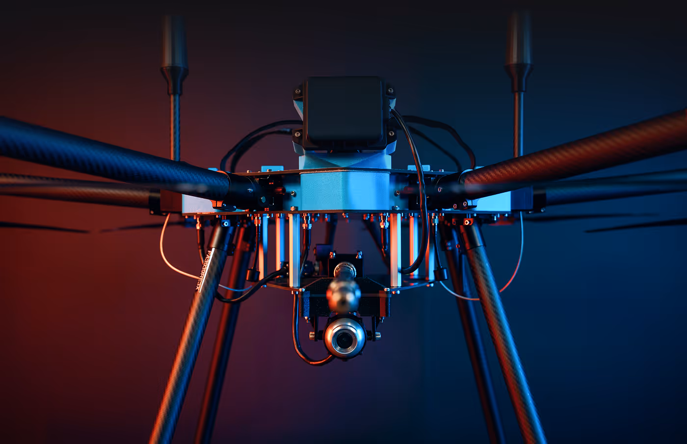 Close-up of a drone with a camera, featuring sleek carbon fiber arms against a vibrant red and blue gradient background, conveying a futuristic feel.
