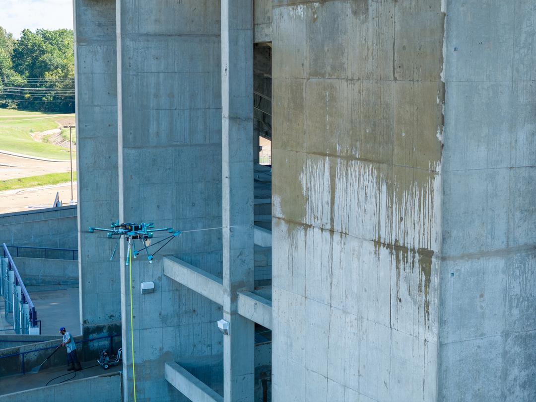 Side view of a drone spraying a sealer on a concrete stadium
