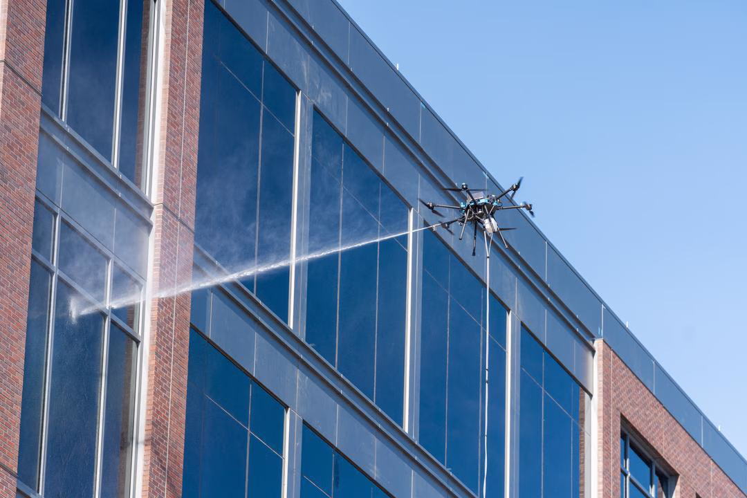 Zoomed out shot from the ground of a drone flying and spraying a window to the left