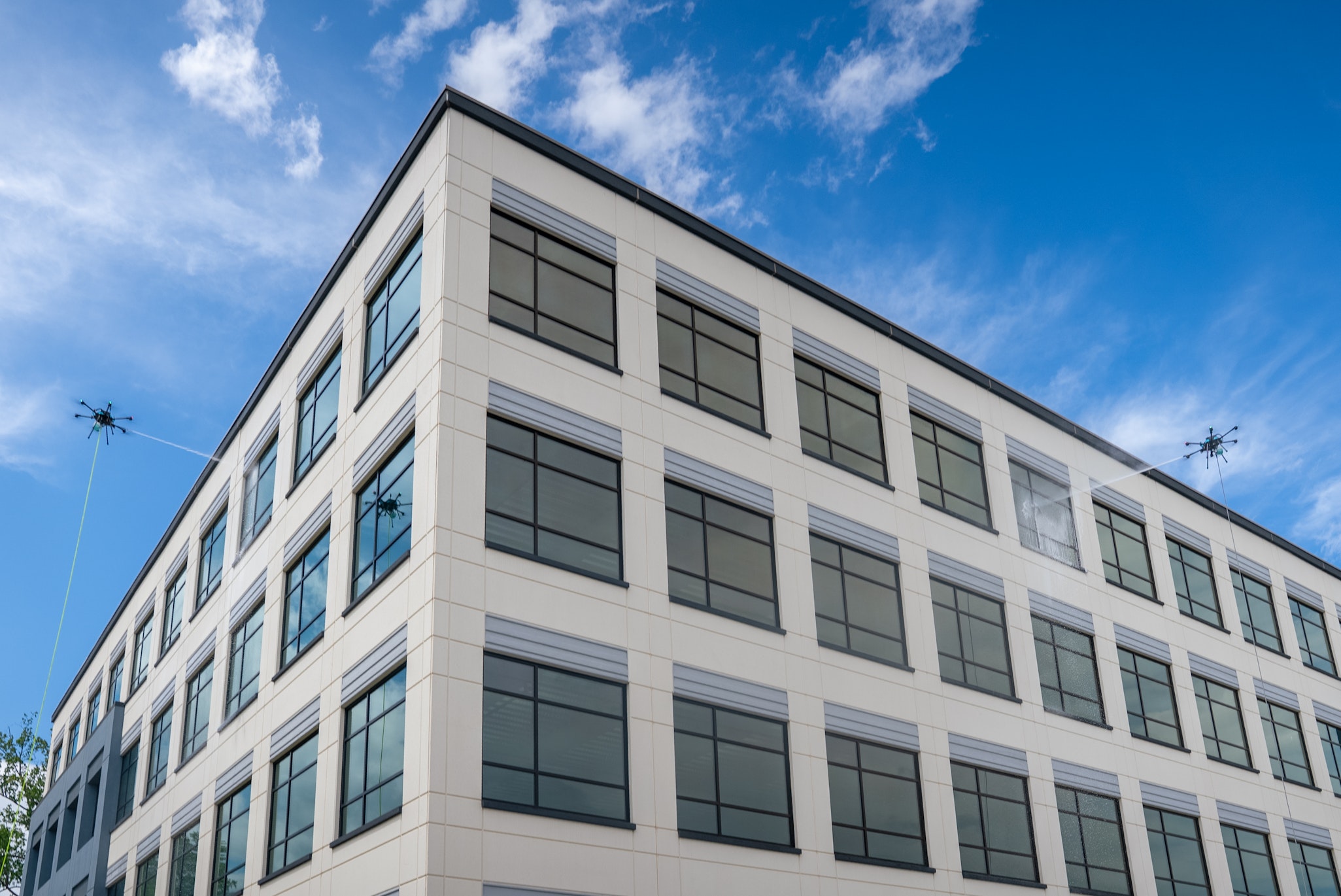 Wide shot of a mid-rise commercial office building with two drones cleaning its exterior
