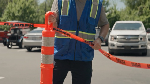 operator in a safety vest setting up caution tape and cones