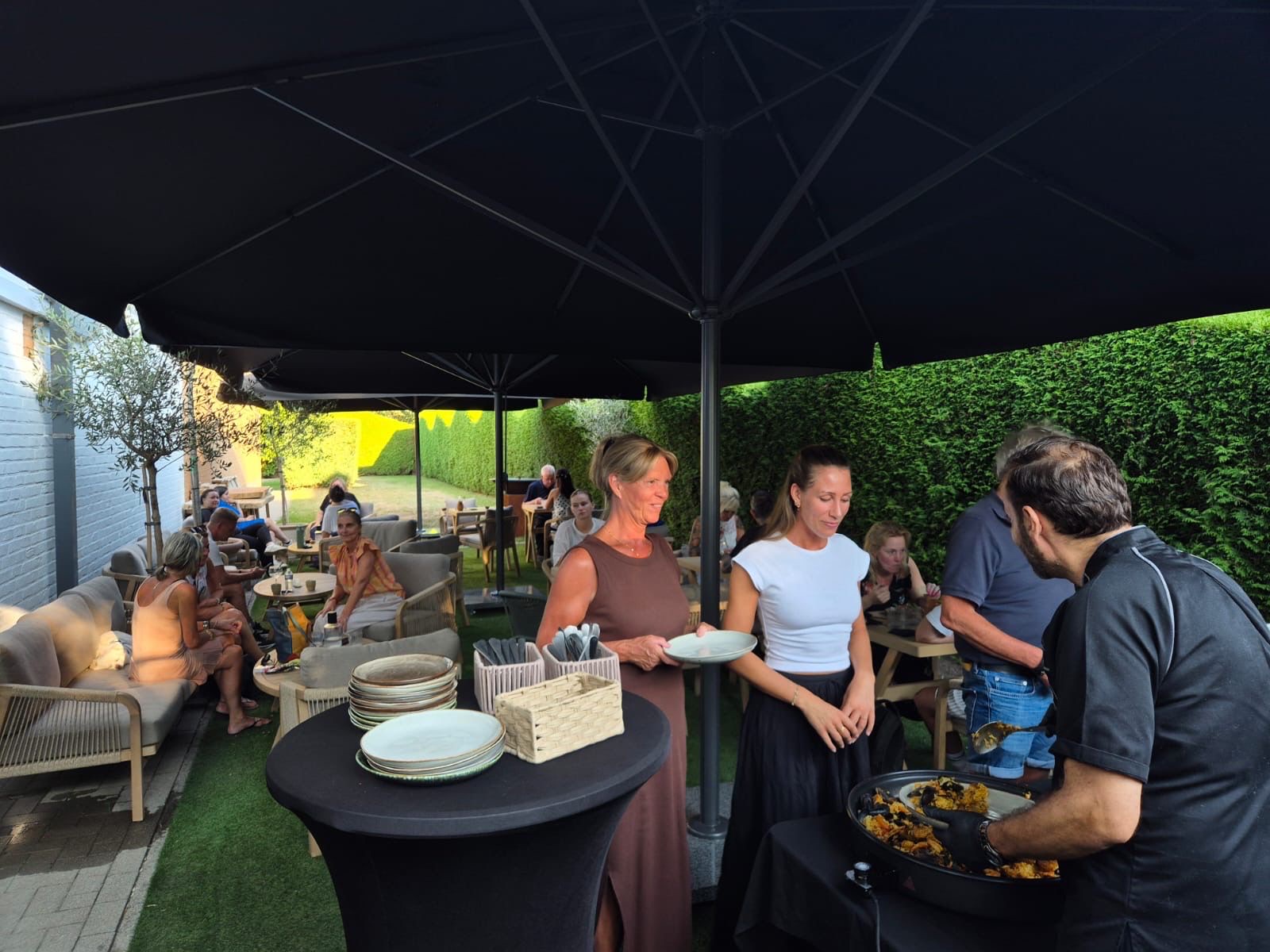 Leden aan het buffet onder de parasols in de tuin