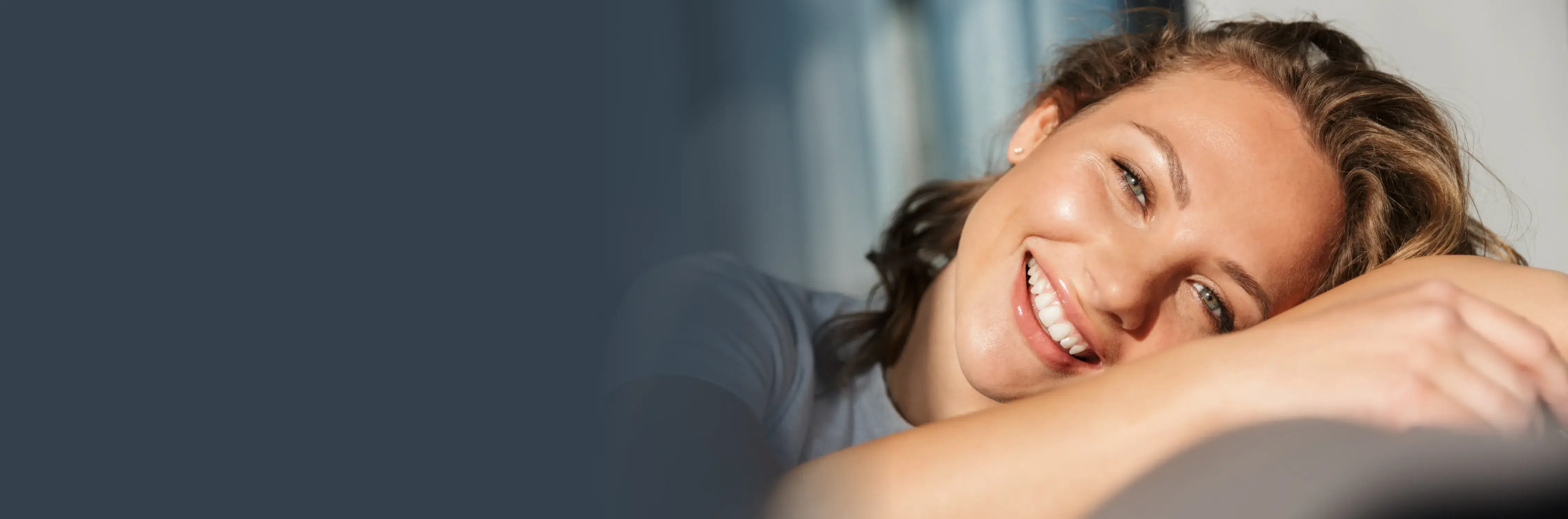 smiling woman sitting on a couch with her arm on her chest Dynamic Dental