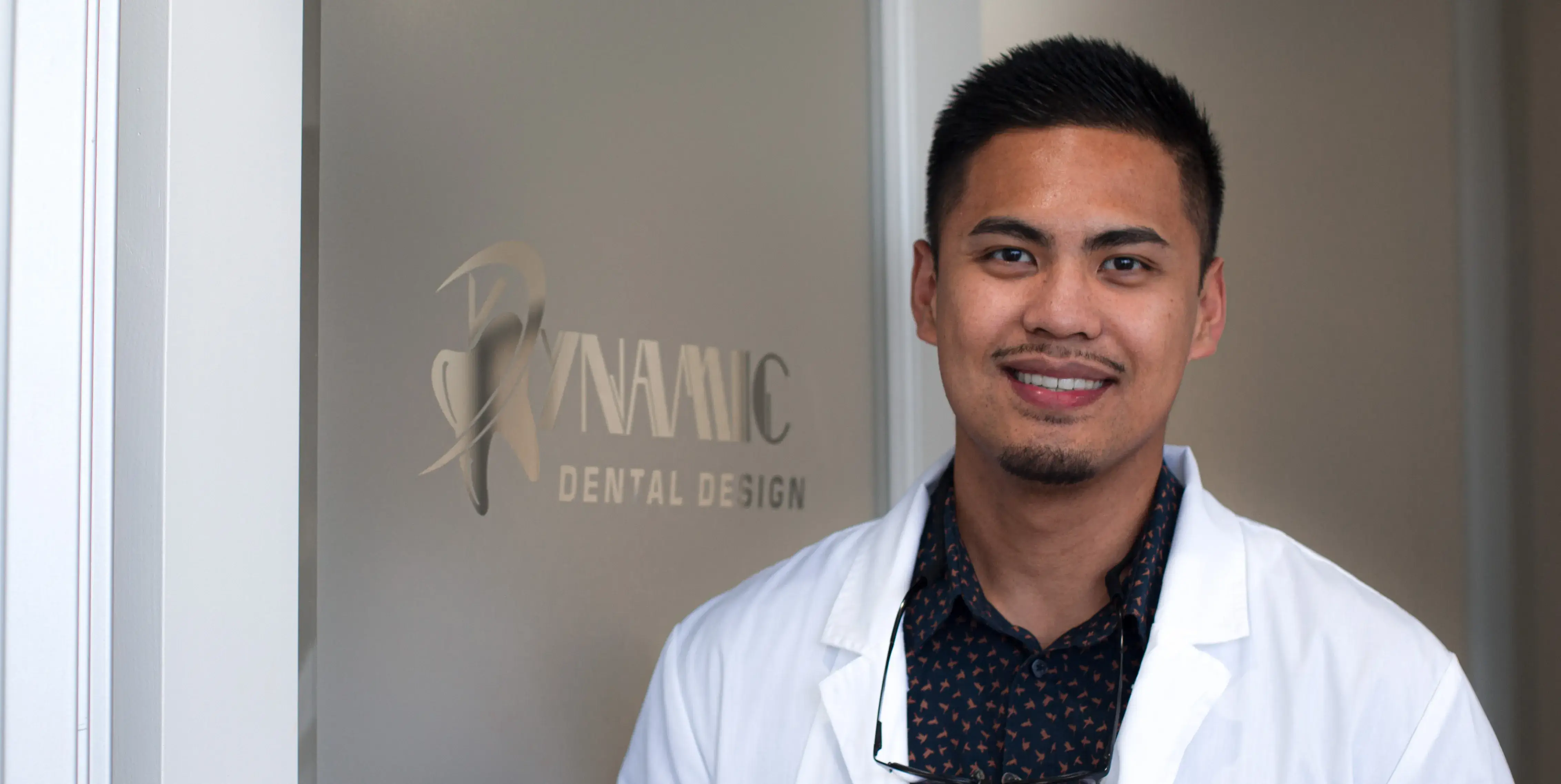 male in a white lab coat standing in front of a sign Dynamic Dental