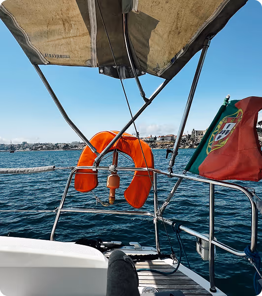 Sailing boat in Cascais Bay with Portuguese flag and life ring, overlooking the coastline on a sunny day.