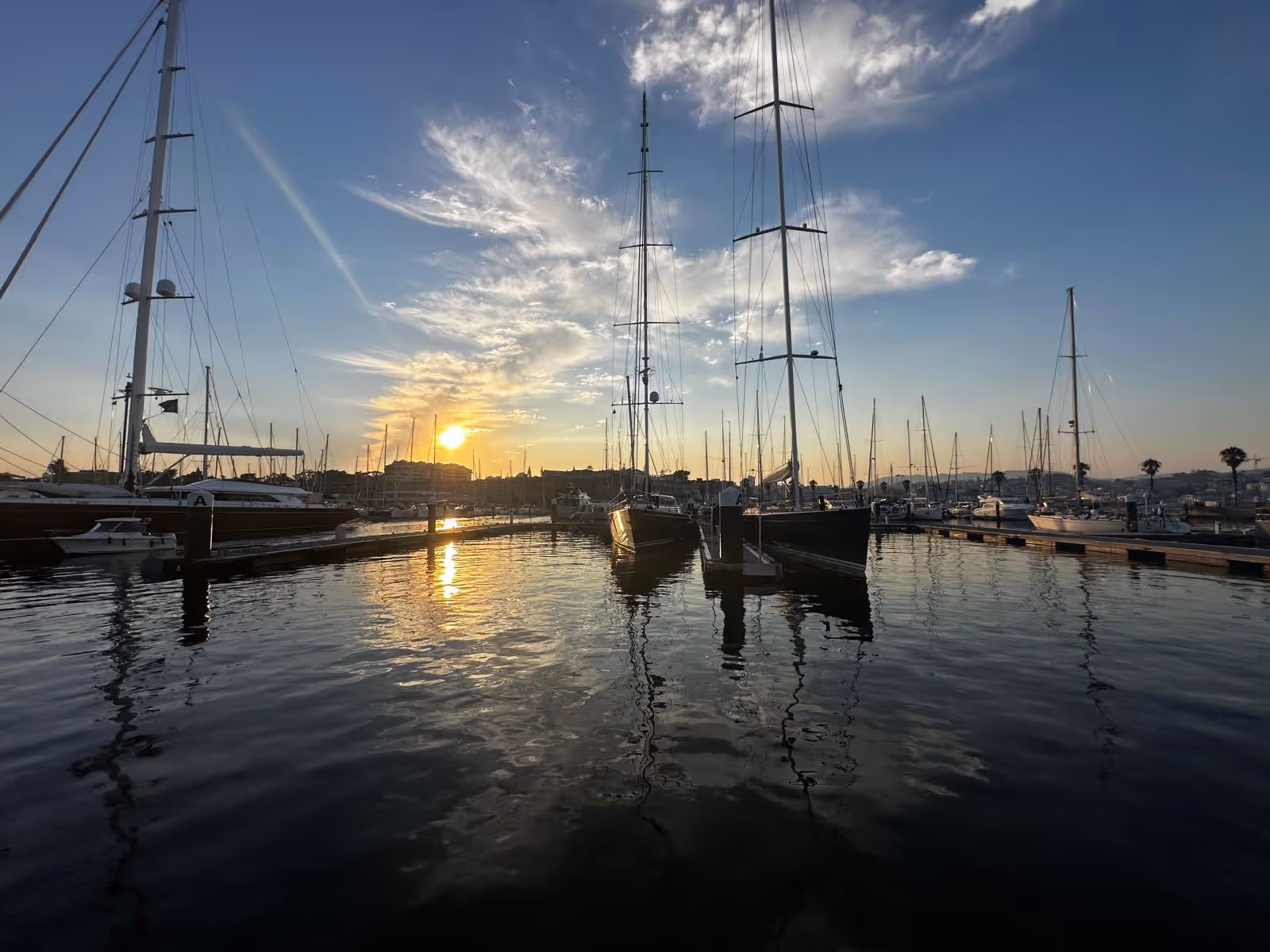 Serene marina at sunset with several docked sailboats and a glowing sky reflecting on the water’s surface.