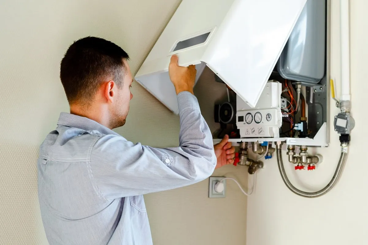 A male technician wearing gloves uses a screwdriver to repair the electrical components of a boiler