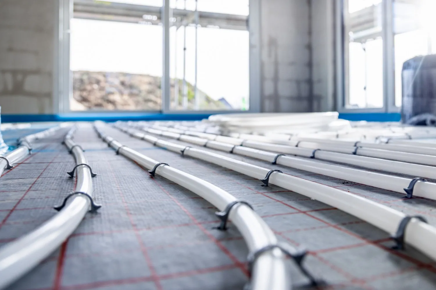 Close-up of white hydronic radiant heating pipes secured with clips to a grid-patterned insulation layer.