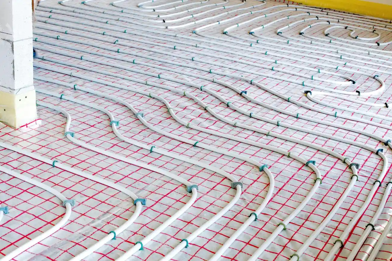 Parallel rows of white hydronic heating pipes secured with clips to a gridded insulation floor.