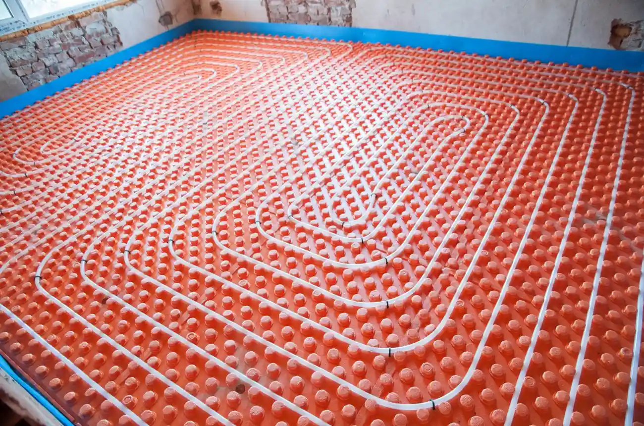 Installation of white hydronic heating pipes in a spiral layout over an orange studded insulation floor.