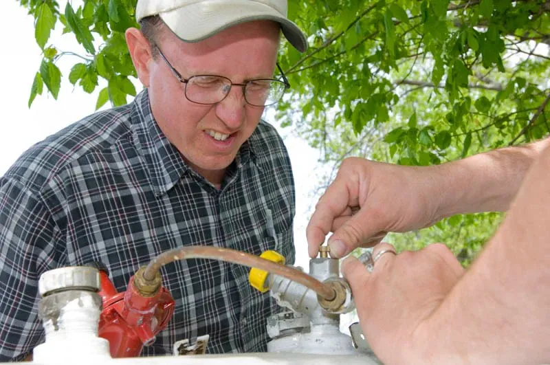 Man inspecting propane tank valve outdoors.