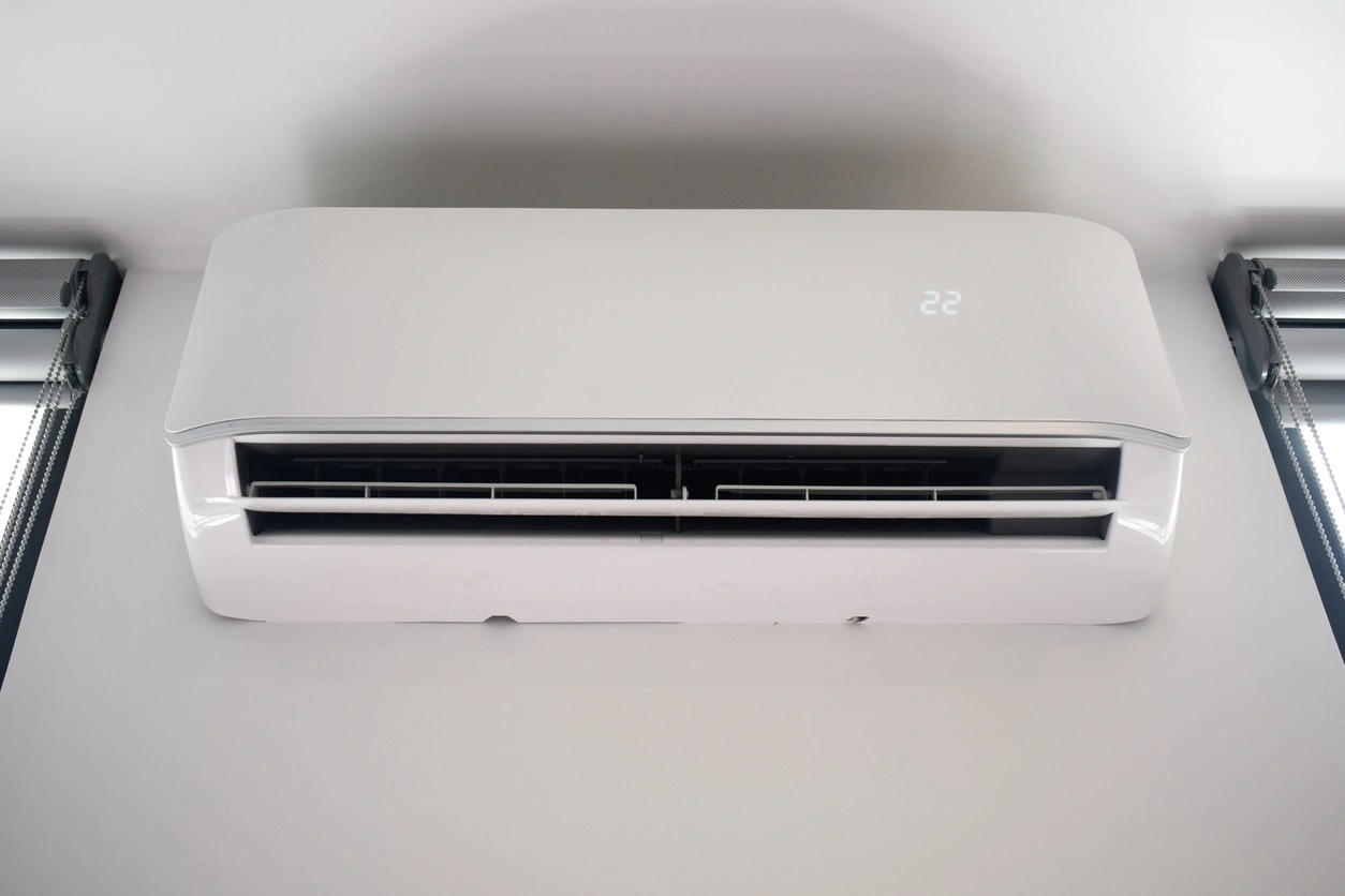 Wall-mounted air conditioner with digital display set to 22°C, positioned between windows with roller blinds.