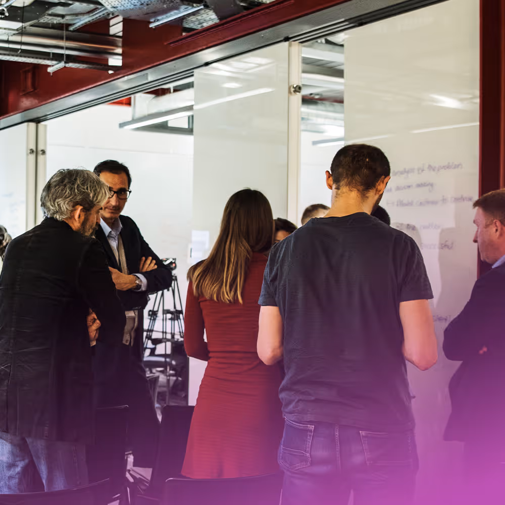 Man with glasses and beard speaking and gesturing with hands during a discussion in a bright room.
