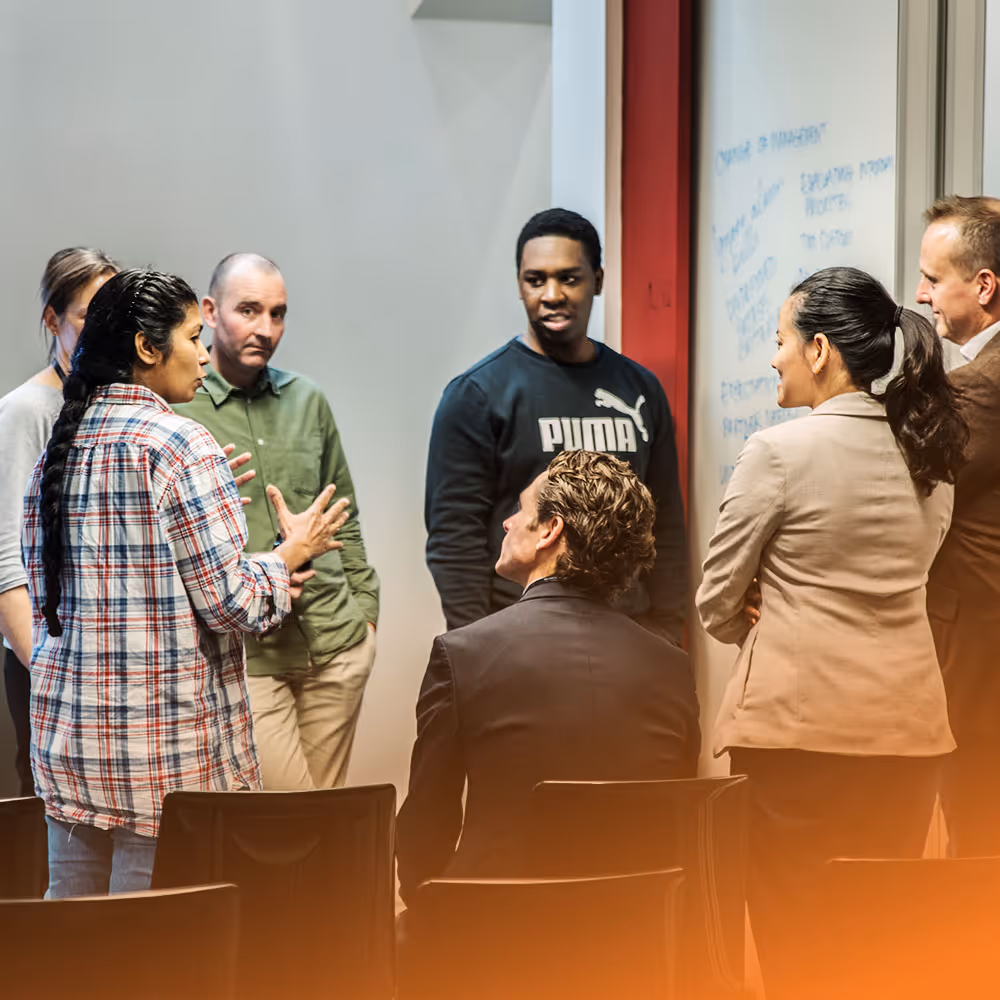 Four colleagues collaborating, with one man writing on a glass wall covered in colorful sticky notes.
