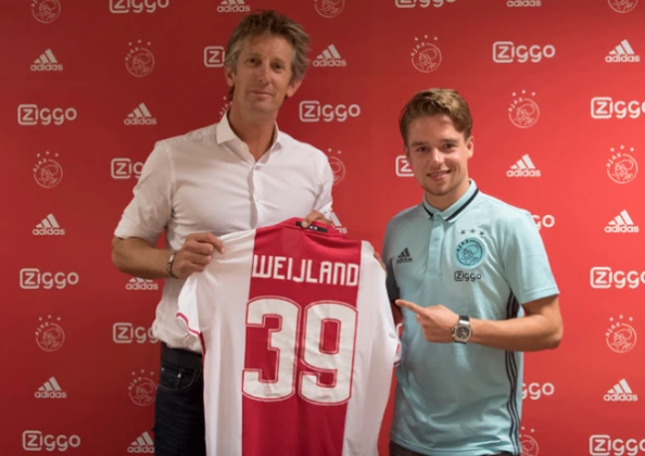 Two men posing in front of a red Ajax backdrop, one holding an Ajax jersey with the name Weijland and number 39 printed on it.