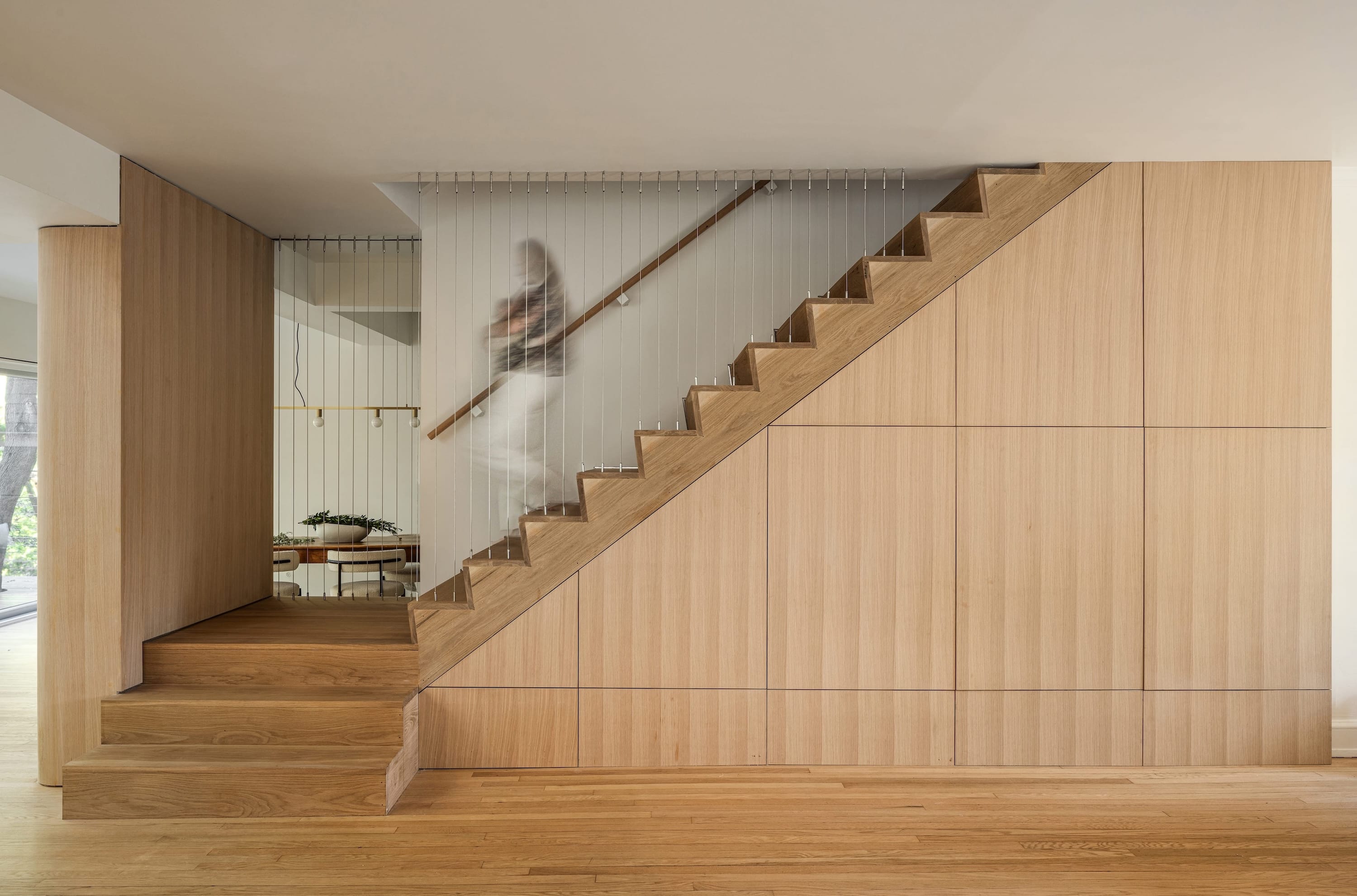 Wooden staircase with vertical cable railing, set against matching wood-paneled walls and floors.