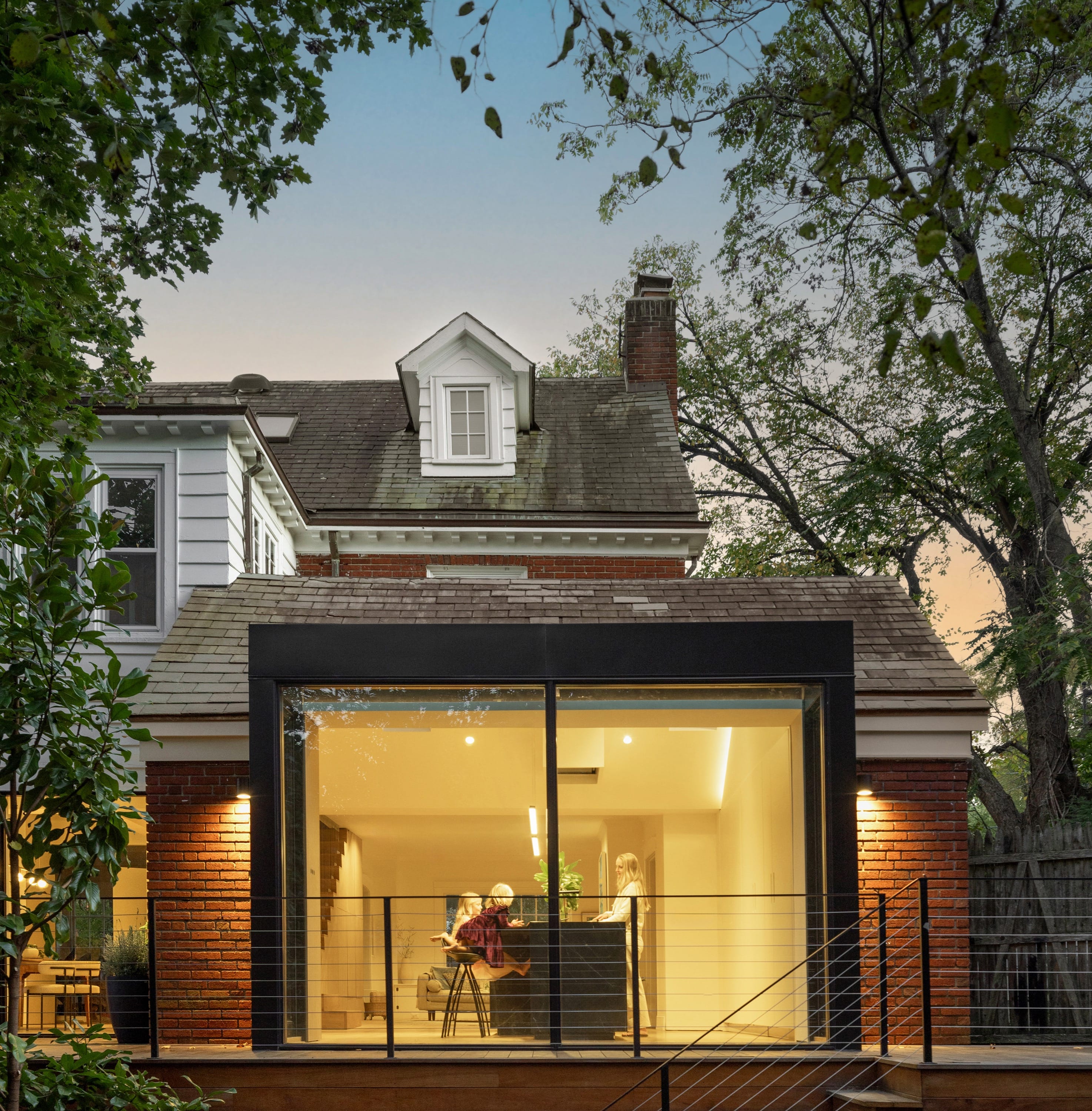 Modern home exterior with glass addition and trees.