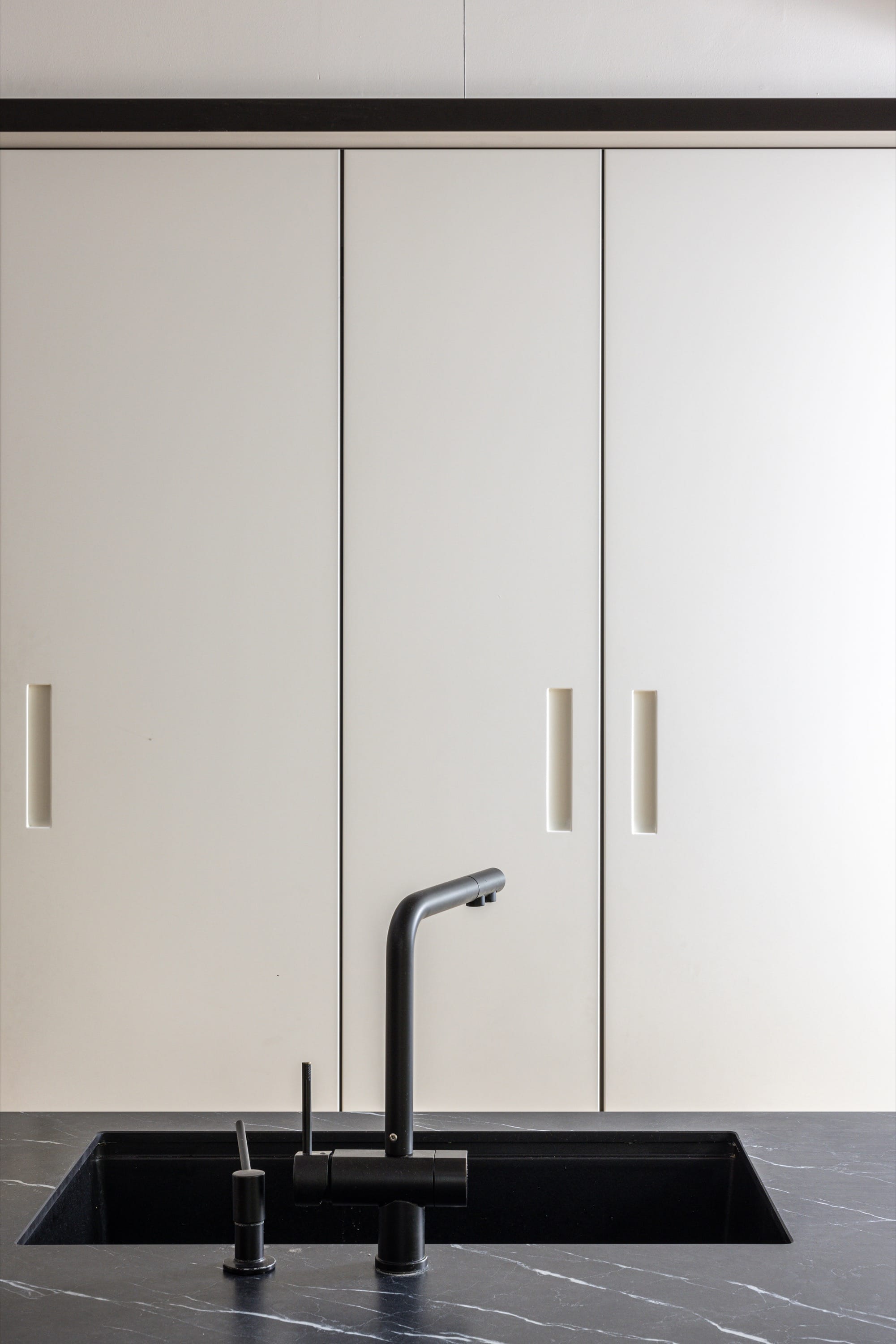 Minimalist kitchen with white cabinets and black sink.