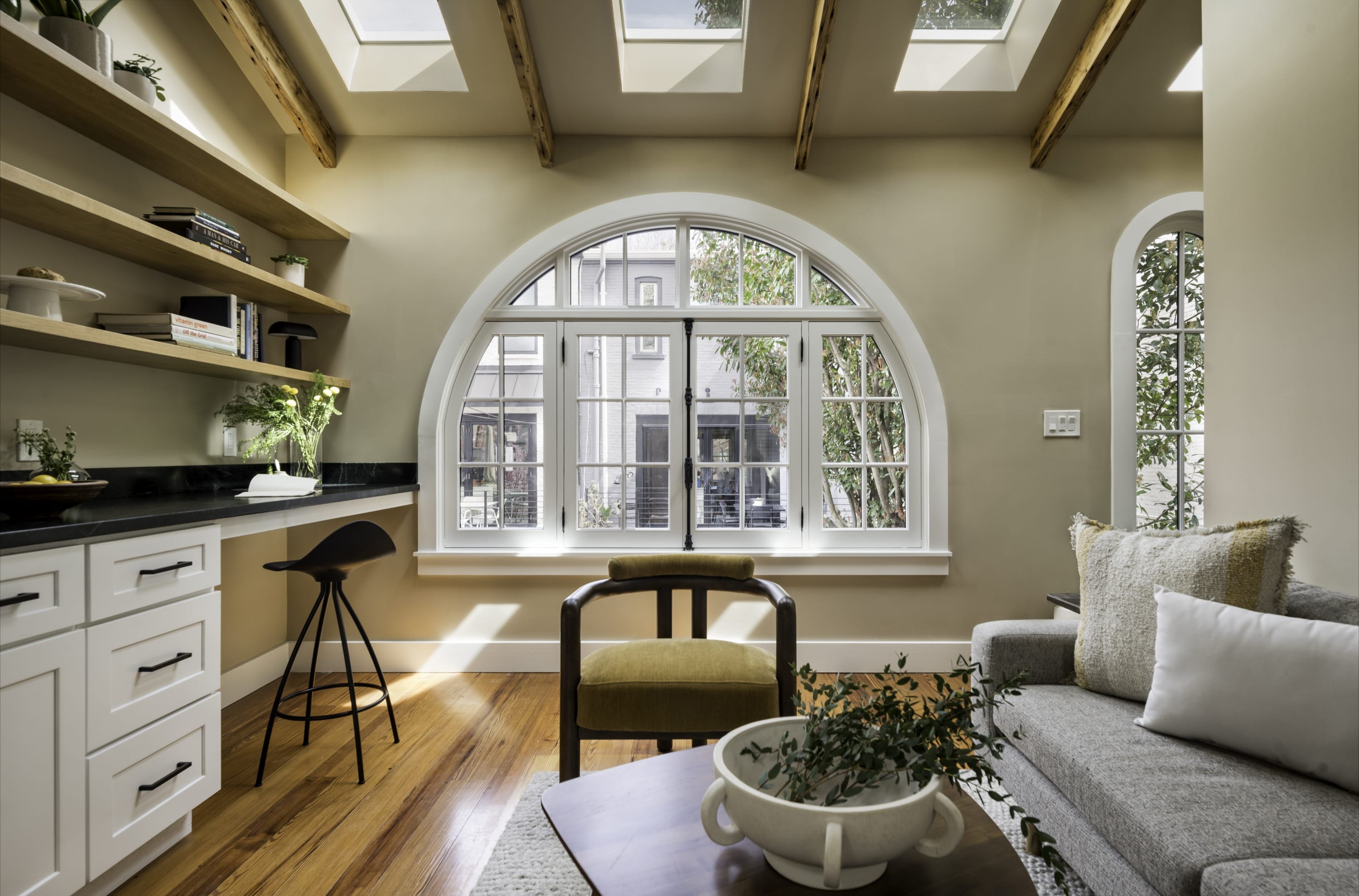 Living room with beams, arched window, and open kitchen.
