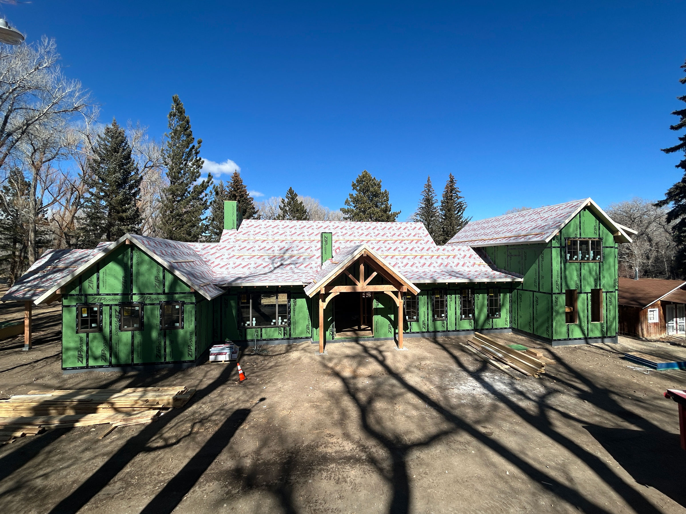 Large custom home in early construction phase with green Zip System sheathing and exposed framing under a clear blue sky