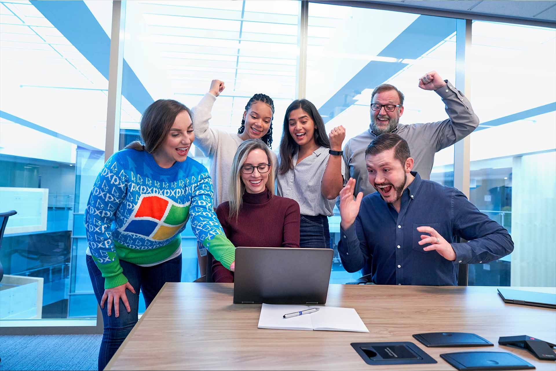 People around a computer and celebrating, representing the idea of unlocking incentives with Microsoft Campaigns.