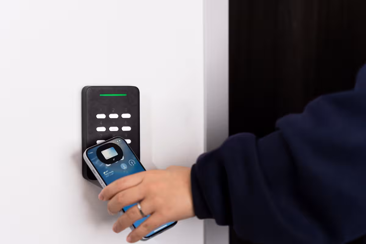 hand holding Apple iPhone in front of keypad unlocking door