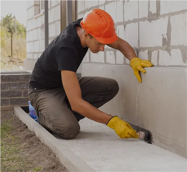 A man is painting the bottom of the house with a paintbrush.
