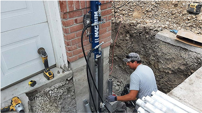 Contractor installing a foundation support pier next to a brick wall of a house.