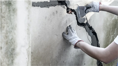 Worker repairing a large crack in a concrete wall using filler material.
