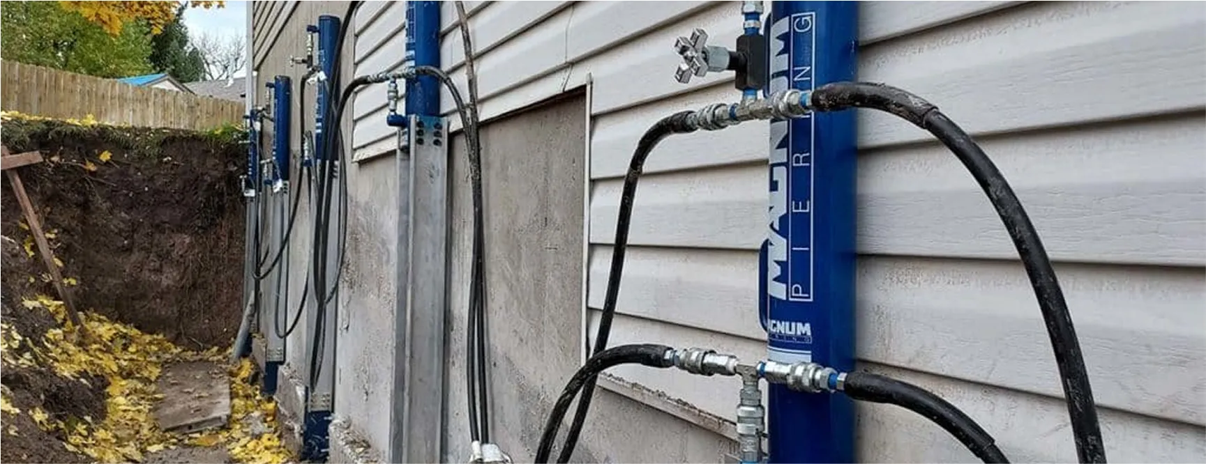 Hydraulic push pier system installed along the foundation wall of a house for structural stabilization.