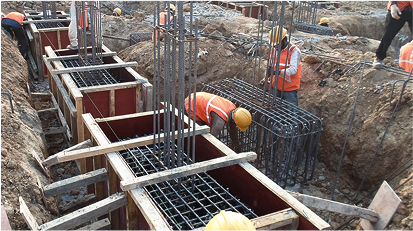 Construction workers building reinforced concrete footings with rebar and forms in a trench.