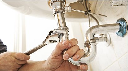 Close-up of a plumber’s hands tightening pipes under a sink using a wrench, focusing on plumbing maintenance