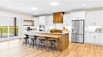 Spacious kitchen with white cabinets, wooden island countertop, and black bar stools, featuring hardwood floors and large windows.