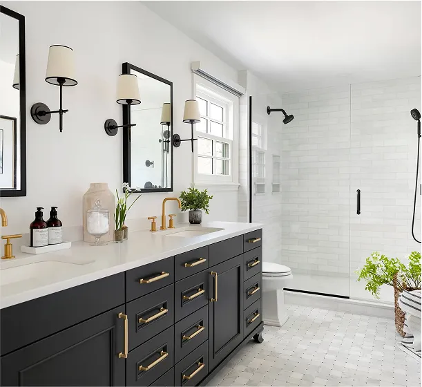 Chic bathroom with dark navy vanity and brass hardware, dual mirrors with black sconces, and a walk-in shower with a white hex tile floor.
