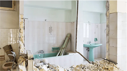 Bathroom under demolition with torn-out tiles, broken walls, and construction debris during renovation.