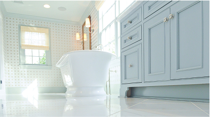 Bright bathroom with soft blue vanity cabinets, a freestanding bathtub, and sunlight streaming through tall windows