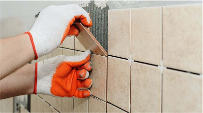 Close-up of a worker's gloved hands installing beige wall tiles with spacers and precise alignment.