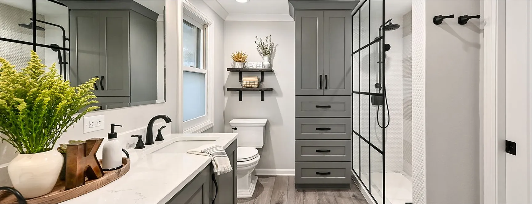 Elegant bathroom with gray vanity cabinets, black fixtures, a quartz countertop, and decorative greenery arranged on the counter for a fresh look