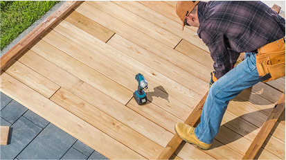 Worker kneeling on a deck while using a drill, repairing or installing wooden deck boards with precision.