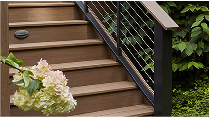 Wooden staircase with modern black metal cable railings and decorative plants, leading down from a deck.