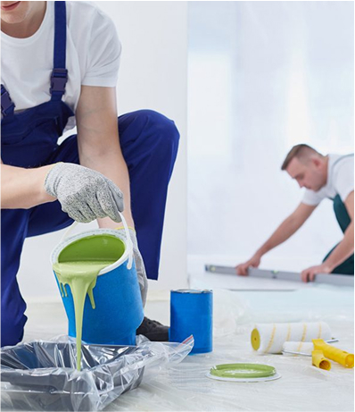 Worker pouring green paint into a tray while another worker measures in the background.