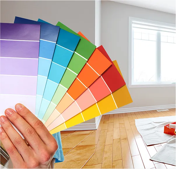 Hand holding a fan of colorful paint swatches in a bright room with hardwood floors and large windows.