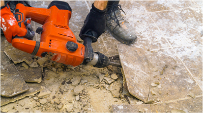 Worker using a demolition tool to remove old flooring and debris.