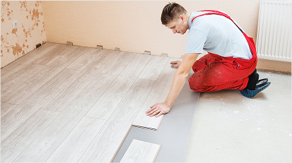Man laying light-colored laminate flooring in a room under renovation.